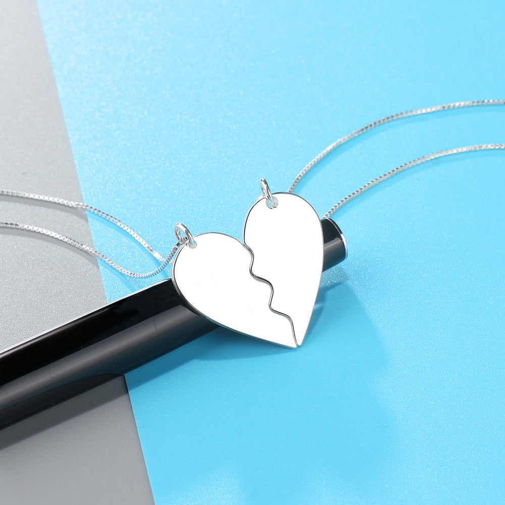 Sterling silver couple necklace with a heart design, split in two, resting on a blue background.